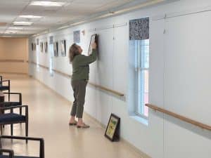 Sunnyside staff members laughing and working together to hang resident artwork in Artist Alley, a creative gallery space inside Sunnyside Retirement Community.