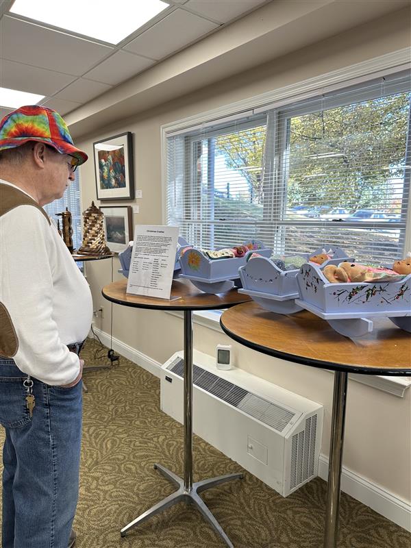 A resident admires hand-painted wooden cradles filled with dolls displayed by a sunny window.