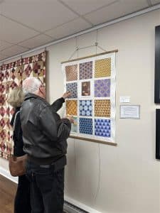 A couple studies a quilted wall hanging featuring geometric patterns and bright colors.